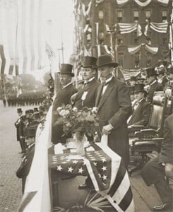 President Theodore Roosevelt, surrounded by flags, reviews a Memorial Day parade in 1907