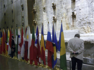 A man bows his head at a World Trade Center wall at the 911 Museum in New York City. National flags are displayed next to him. (James Breig photo)