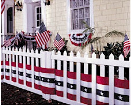 Front of home decorated with American flags, pleated fans and a fence with bunting