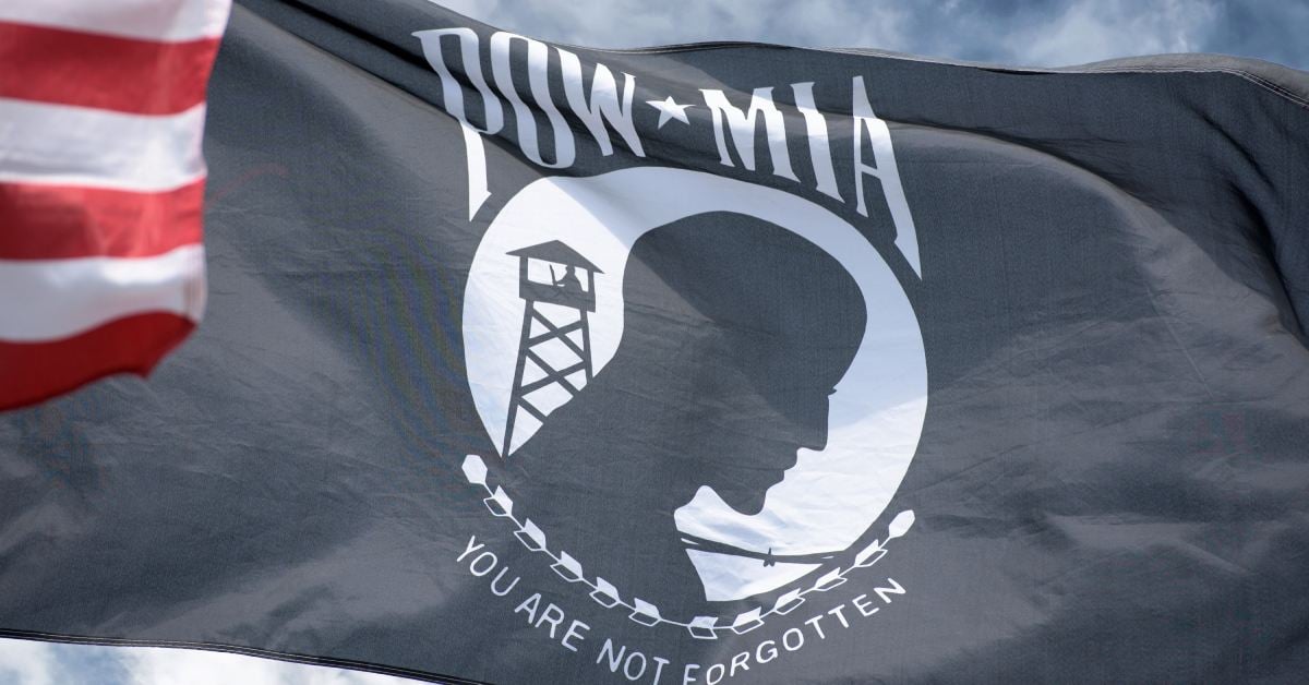 pow/mia flag waving in the wind, with a blue/grey sky behind, the edge of an american flag peeking from the corner